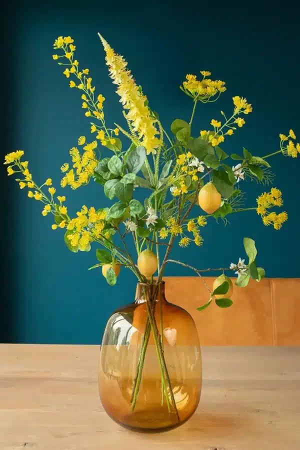 Jula Bloom’s Ghandi silk flower bouquet with yellow blooms and hanging lemons, in a semi opaque brown glass vase on a table