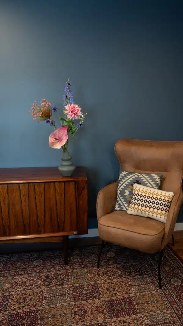 Jula Bloom’s Robinson silk flower bouquet with purple and pink blooms, in a grey vase on a table with a brown leather chair