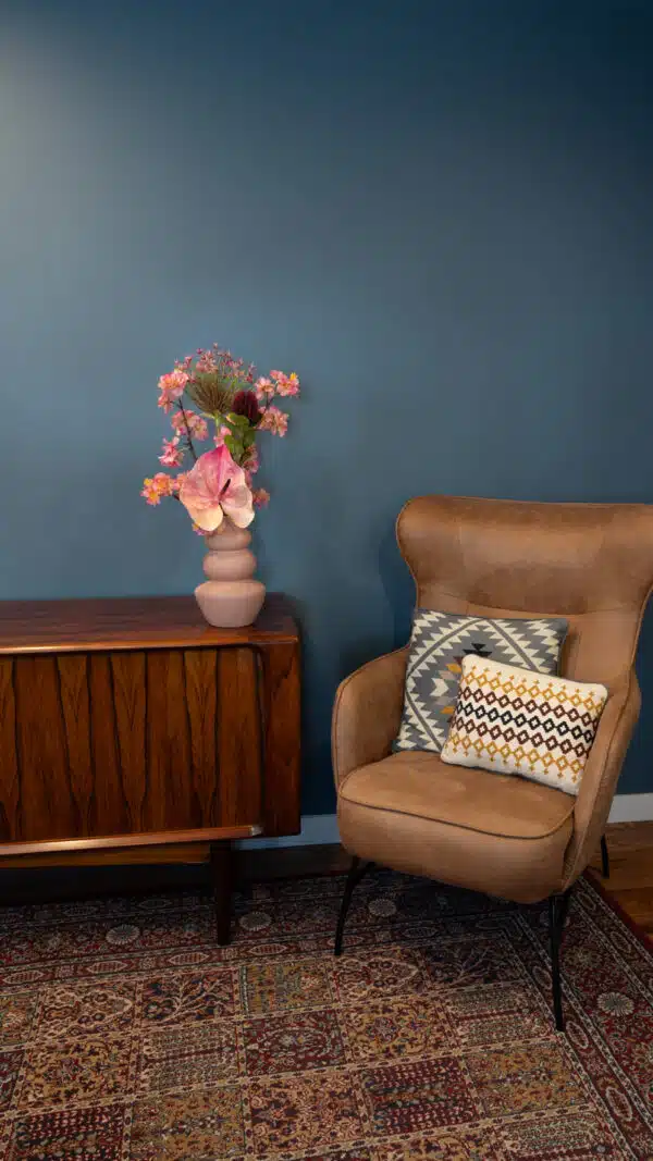 Jula Bloom’s Jacobs silk flower bouquet with pink and red blooms, in a pink vase on a side table with brown leather chair