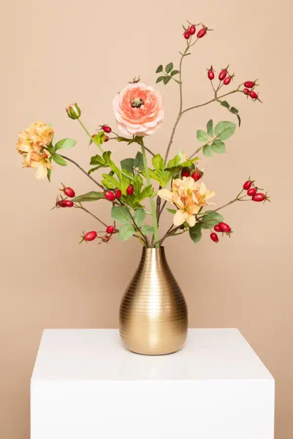 Jula Bloom’s Malala silk flower bouquet with pink and orange blooms, red buds and green leaf, in a gold sheen vase, on a white pillar