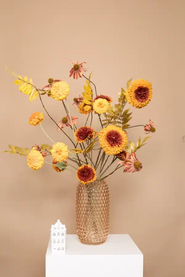 Jula Bloom’s Goodall silk flower bouquet with burnt orange and red blooms and gold leaf, in a opaque studded brown vase, on a white pillar