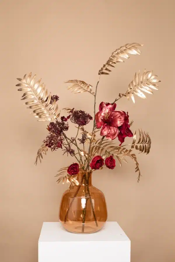 Jula Bloom’s Angelou silk flower bouquet with deep red blooms and gold leaf, in a opaque brown vase, on a white pillar