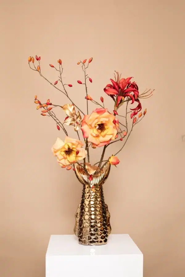 Jula Bloom’s Aubigny silk flower bouquet with red, yellow and pink blooms, red buds and gold leaf, in a gold fish vase on a white pillar